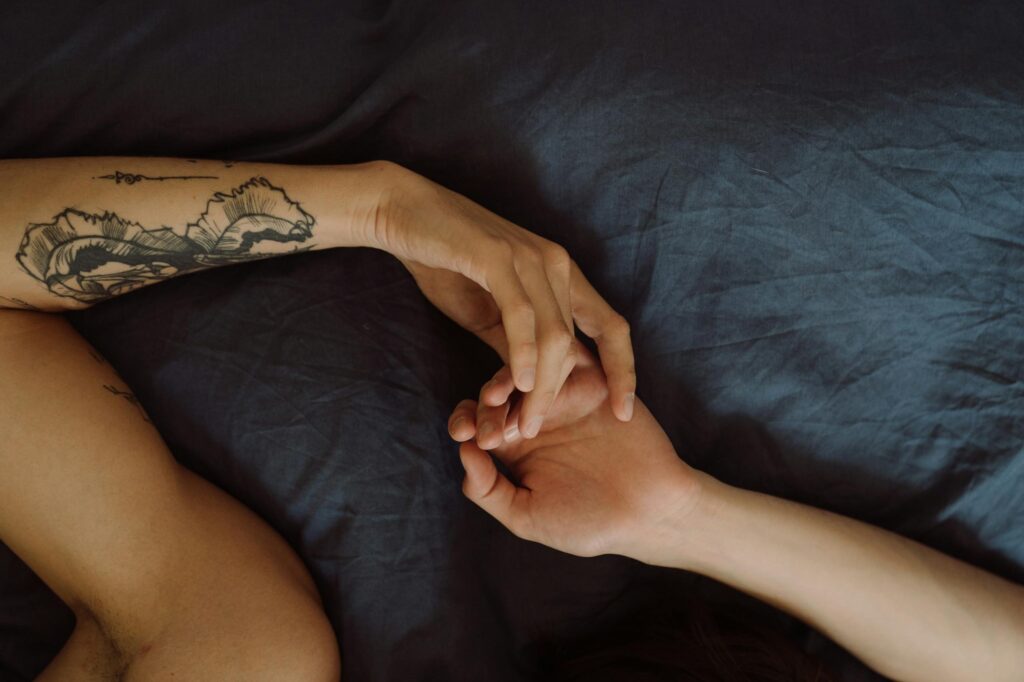 A tattooed arm holding hands in an intimate setting, symbolizing love and tenderness.
